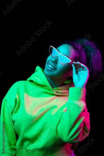 Stylish. African-american woman's portrait isolated on dark studio background in multicolored neon light. Beautiful female model. Concept of human emotions, facial expression, sales, ad, fashion.