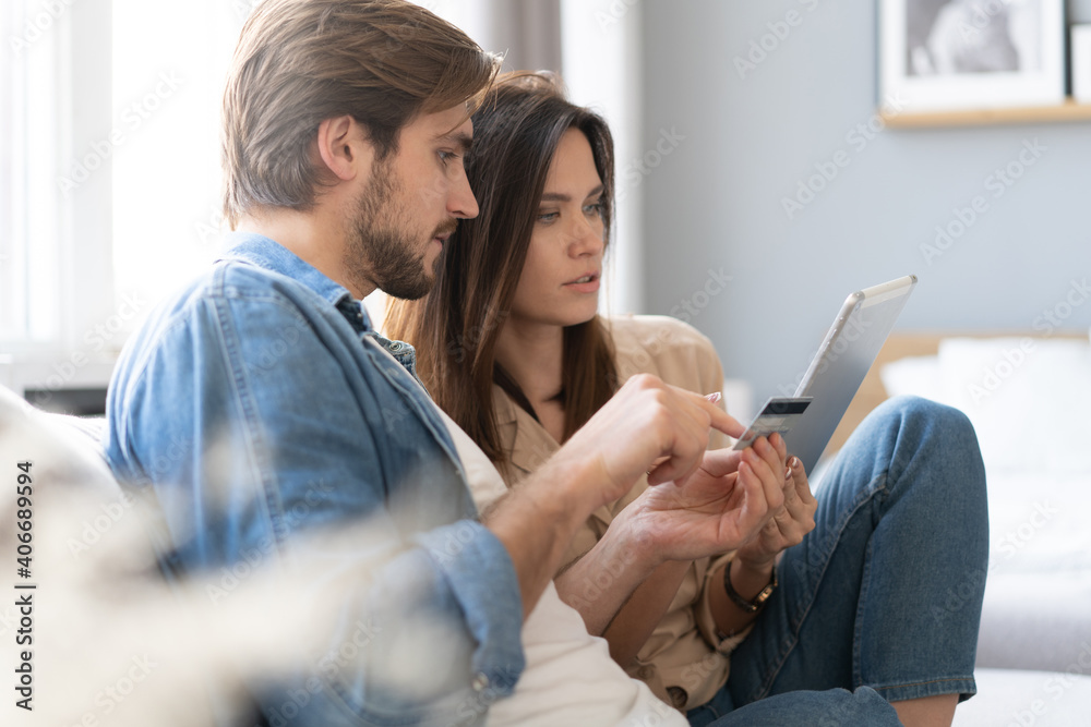 Obraz premium Laughing couple sitting on the couch shopping online with tablet pc at home in the living room.