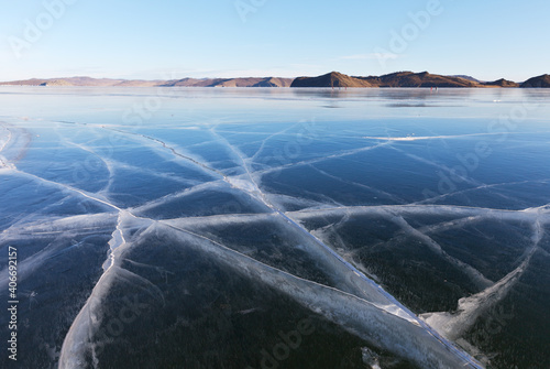 Frozen Baikal Lake on a sunny winter day. Natural background with blue snowless ice with cracks in the Small Sea Strait. Beautiful  winter landscape. Ice travel. Close-up view