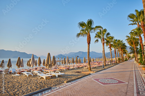 Fototapeta Naklejka Na Ścianę i Meble -  sandy beach without people and with sun loungers, folded umbrellas, palm trees, Turkey