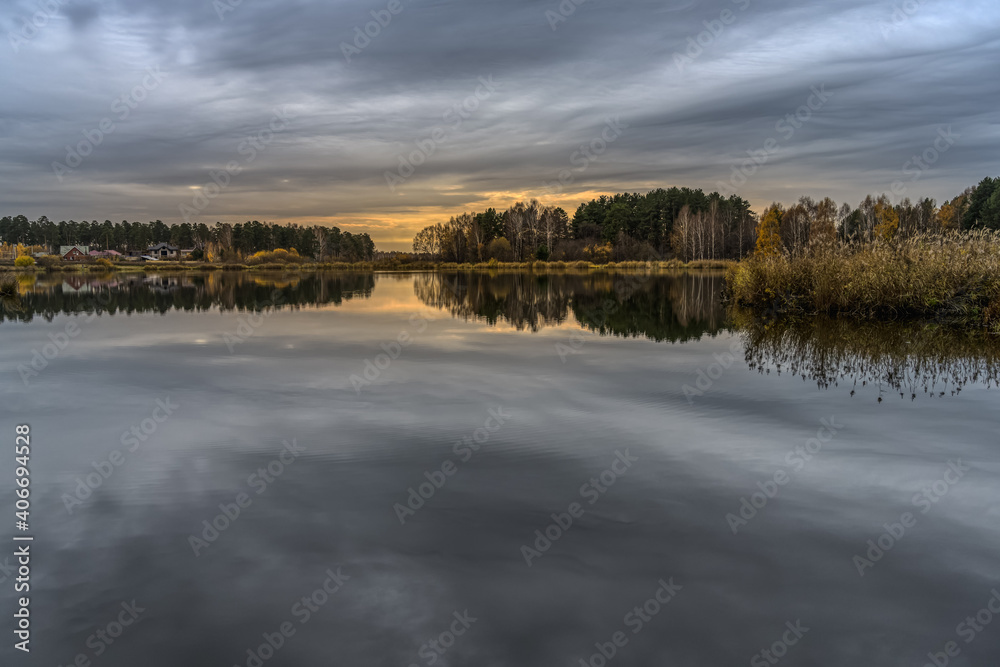 lake in the autumn morning. between sky and water. reflection of gray cloudy sky in calm water. in the distance village houses are visible, autumn colors in nature.