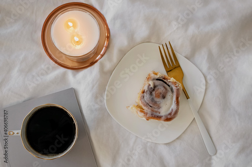 Lifestyle composition with cinnamon bun, coffee and burning candle