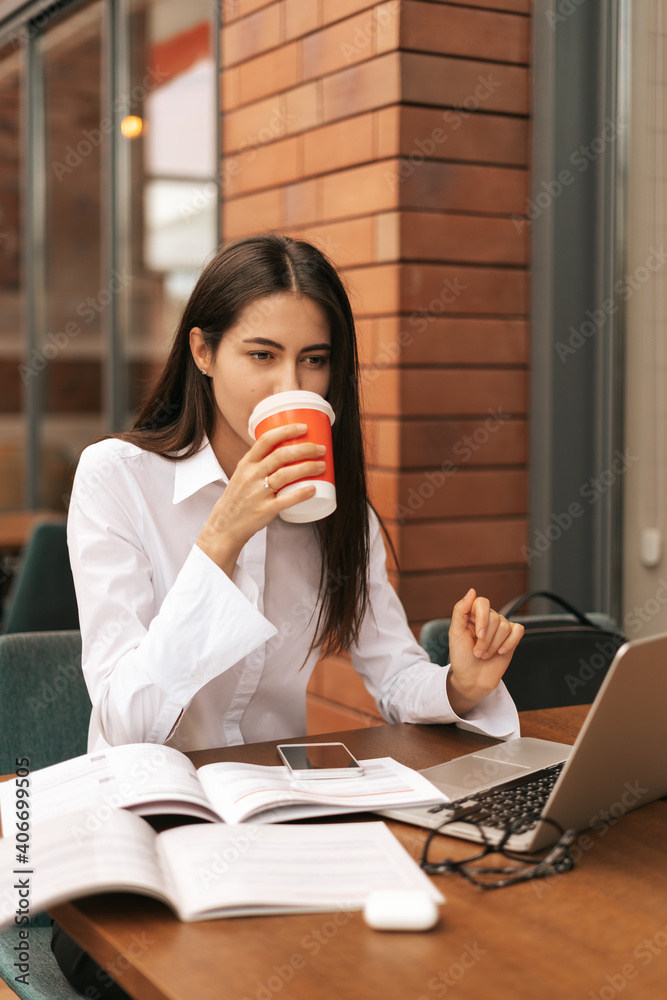 Smiling businesswoman enjoying take away coffee while working in a cafe on a portable computer connected to public WiFi. Smiling businesswoman enjoying take away coffee while working in a cafe on a portable computer connected to public WiFi.