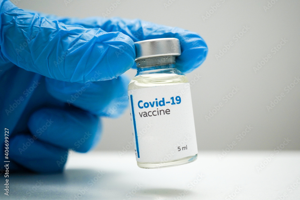 Doctor's hands in blue medical gloves holding a dose of coronavirus vaccine in a glass bottle. Liquid Covid-19 disease treatment for injections. Immunization against corona illness concept.