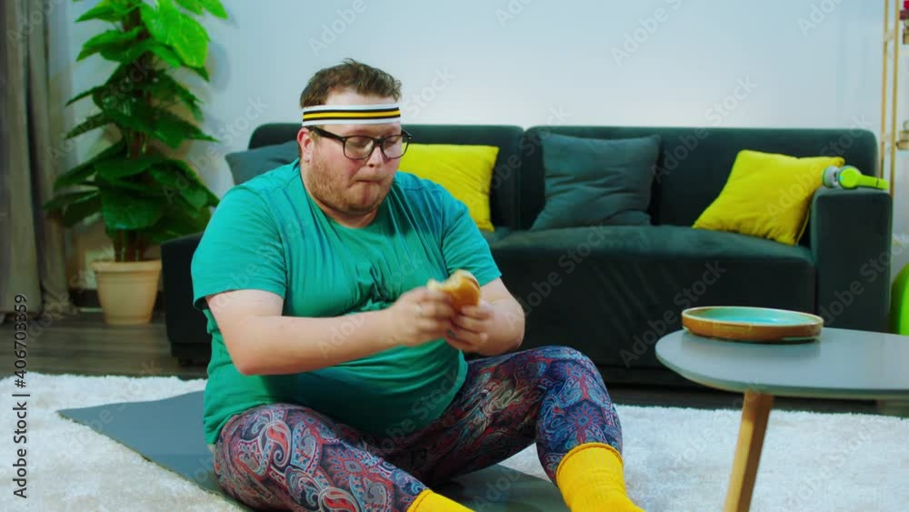Fat guy have a workout at home in the living room he doing crunches then take a bit of hamburger and continue to do the workout