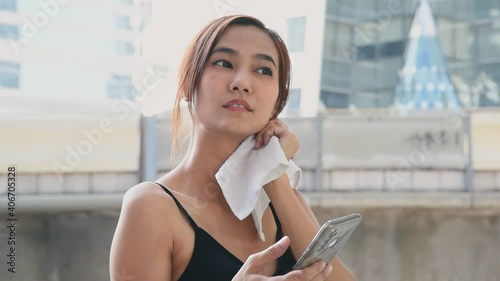 Asian woman in sport outfit take a break and using smart phone after running workout in the city with metropolis background