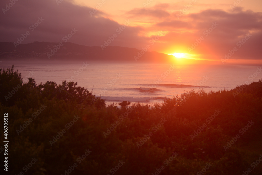 Golden red sunrise over the ocean with perfect rolling waves for morning surfing with the view of the mountains 