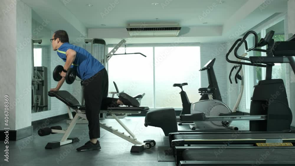 Young Asian man in sportwear pick up and doing one-arm dumbbell rows on bench in gym. sport, bodybuilding, fitness and people concept Young Asian man in sportwear pick up and doing one-arm dumbbell rows on bench in gym. sport, bodybuilding, fitness and people concept