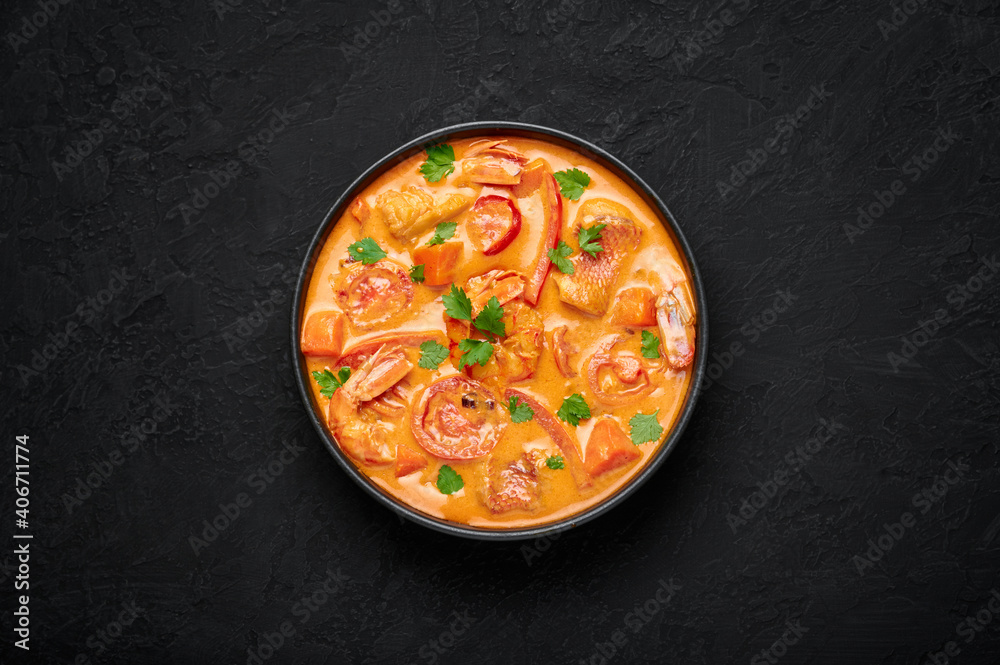 Moqueca with Fish and Shrimps in black bowl on dark slate table top. Brazilian sea food curry dish with coconut milk and vegetables. Top view