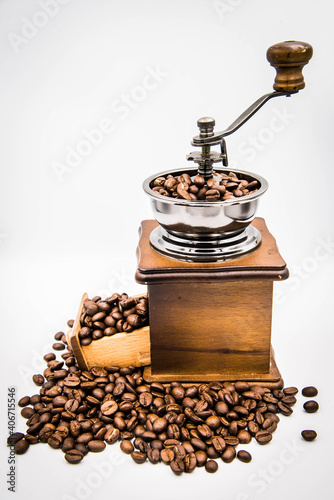 
A traditional hand-cranked coffee grinder, coffee beans overflow from the drawer and cone grinders.