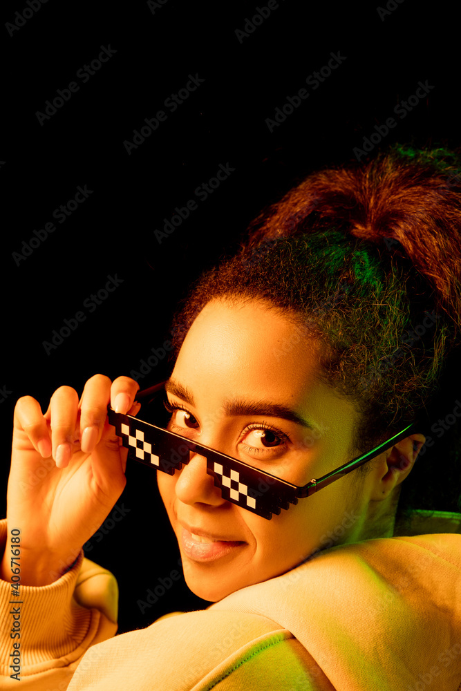 Obraz premium Look back. African-american woman's portrait isolated on dark background in mixed neon light. Wearing trendy pixel eyewear. Concept of human emotions, facial expression, sales, ad, fashion. Copyspace.