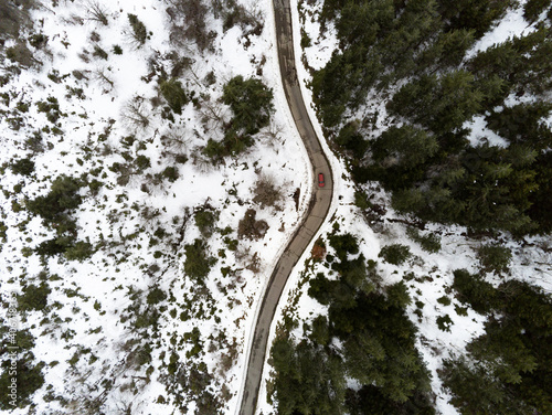 Aerial drone view of a mountain in winter with snow cut by a road with a red car passing by on the street © loreanto