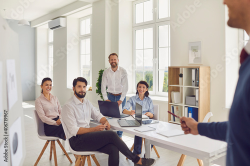 Young man discussing something while his colleagues listen to him sitting at an office desk.