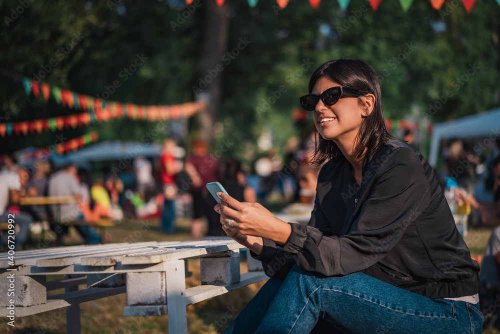 Obraz premium Beautiful female using mobile phone on sunny day on outdoor street fair parade festival