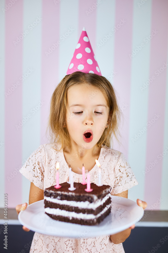 Foto de Little girl in pink cap blowing out candles on a birthday
