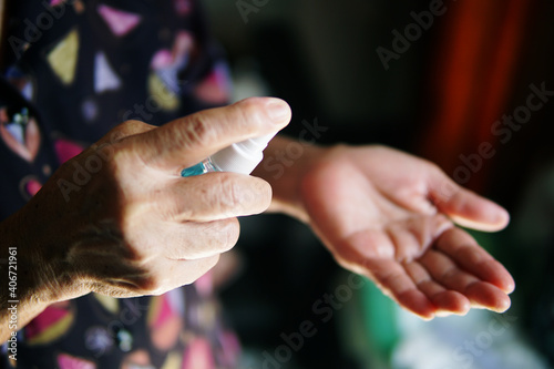 Hand of the elderly woman with alcohol spray bottle.