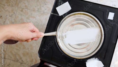 Obraz na plátně Hand holding a metal spoon trying to pry open the lid of a big metal biscuit tin, using the spoon as a lever