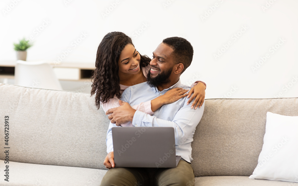 Happy african american couple sitting on couch, using laptop Happy african american couple sitting on couch, using laptop
