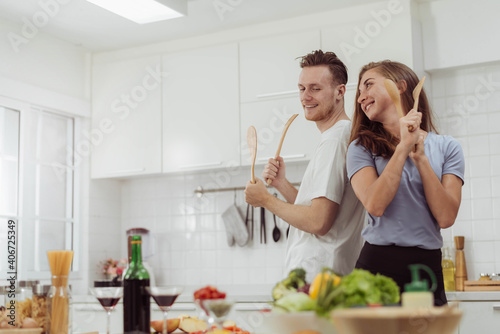 Young Beautiful couple love is dancing while cooking together in the kitchen. Happy loving man and woman cooking healthy food at home.