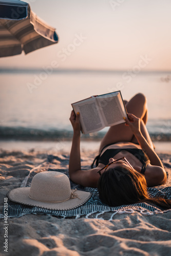 Foto Young beautiful woman sitting on beach reading a book