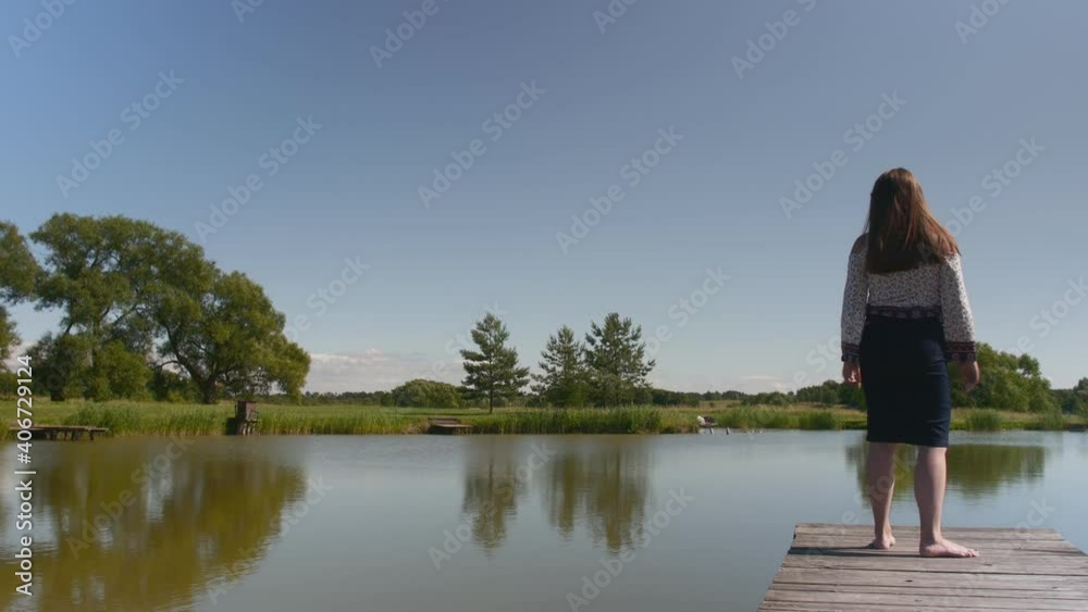 Back view of young happy woman standing and relaxing on the pond in summer Back view of young happy woman standing and relaxing on the pond in summer