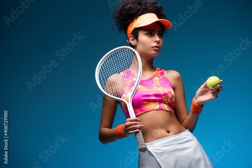 sportive and curly woman holding tennis racket and ball on blue © LIGHTFIELD STUDIOS