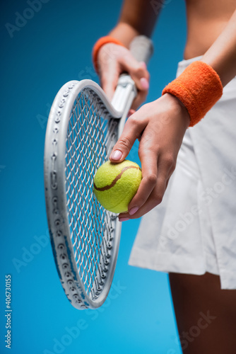 cropped view of sportive young woman holding tennis racket and ball while playing on blue © LIGHTFIELD STUDIOS