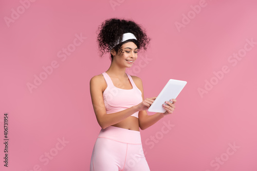 cheerful sportswoman using digital tablet isolated on pink