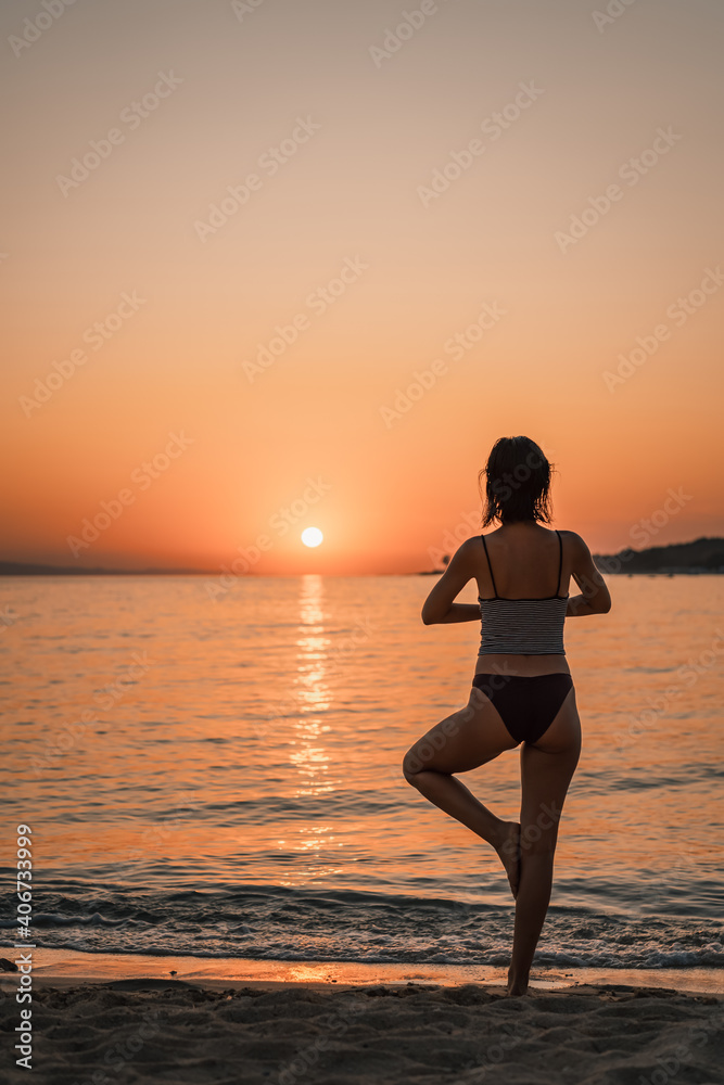 Young beautiful woman practicing pose from yoga on the beach at sunset. Female on beach exercising on vacation