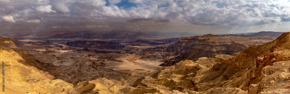 A desert canyon scene with dramatic drop and mountains and heavy cloudy sky. Timna Crater, Israel