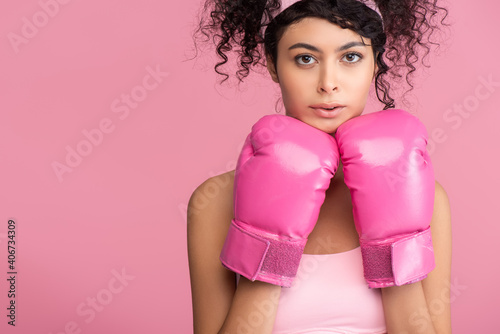 young sportswoman in sportswear and boxing gloves looking at camera isolated on pink