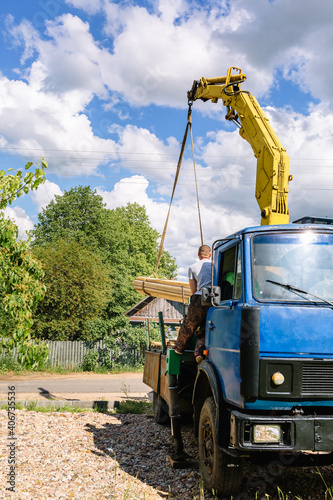 Billede på lærred A blue cargo loader with a manipulator unloads the delivered building material at a construction site