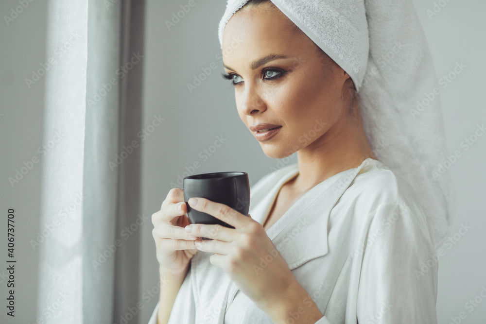 Young woman in bathrobe drinking coffee and looking through the window. Young woman in bathrobe drinking coffee and looking through the window.