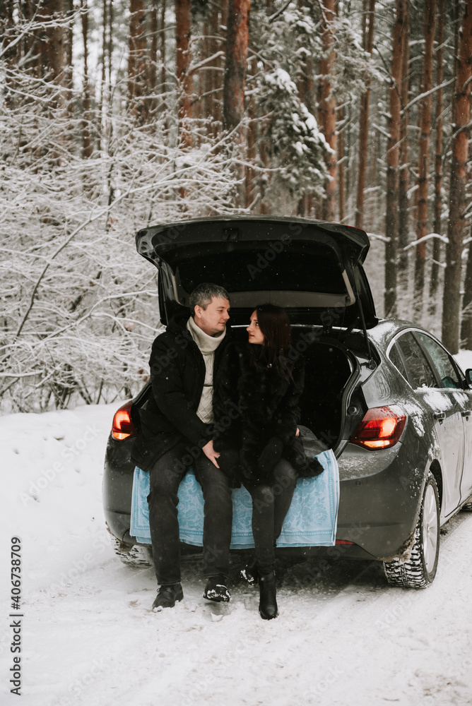 A man and a woman on the background of a snow-covered forest in a snowfall in the trunk of a car