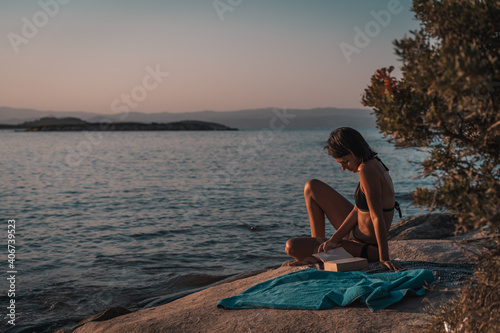 Leisure in summer, young women lying on a beach. Female relaxing with book. Sea in the background. Summer vacation reading concept. Vintage color tone © Vladimir Borovic