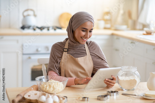 Cheerful Muslim Lady In Hijab Using Digital Tablet In Kitchen