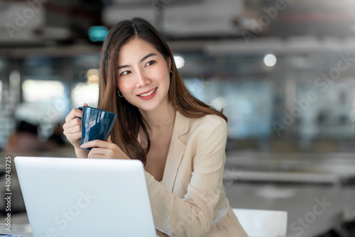 Asian business women sit in the office and drink coffee look laptop computer 