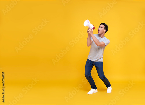 Young Asian man shouting into megaphone making announcement in isolated on yellow background. photo