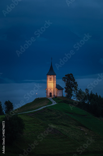 Jamnik, Slovenia - Blue hour at Jamnik with illuminated St. Primoz hilltop church on a foggy dawn. Julian Alps at background