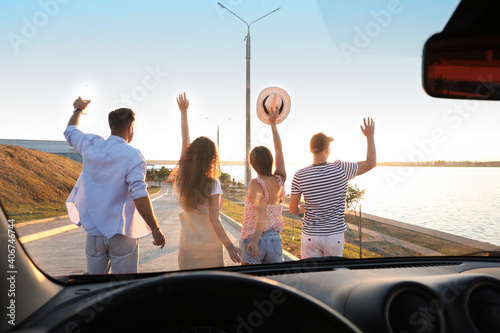 Group of friends near car outdoors at sunset, view through windshield. Summer trip © New Africa