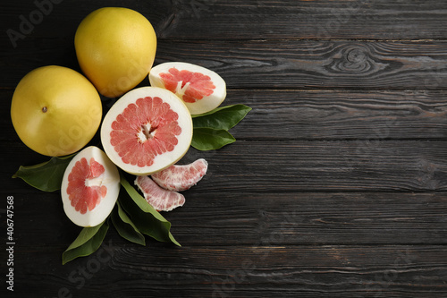 Fresh cut and whole pomelo fruits on black wooden table, flat lay. Space for text photo