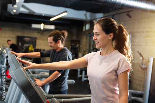 Young fit man and beautiful brunette exercising on the treadmill in modern fitness gym.
