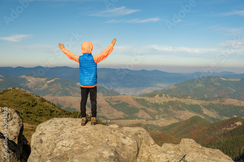 Young child boy hiker standing with raised hands in mountains enjoying view of amazing mountain landscape at sunset.