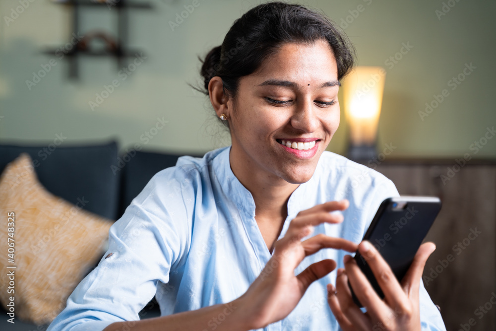 Happy young girl smiling by reading funny message or sms on smartphone - Concept of using social media, online messaging app, Internet and entertainment lifestyle Happy young girl smiling by reading funny message or sms on smartphone - Concept of using social media, online messaging app, Internet and entertainment lifestyle