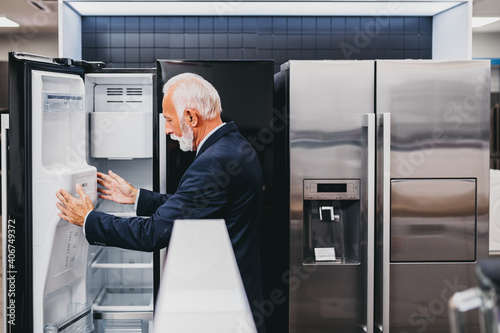 Senior bearded customer choosing fridge in appliances store.