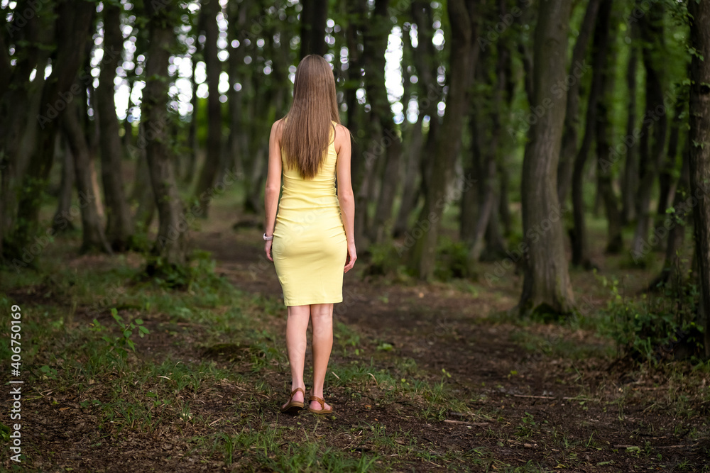 Back view of a slim woman in yellow dress standing in moody dark forest. Back view of a slim woman in yellow dress standing in moody dark forest.