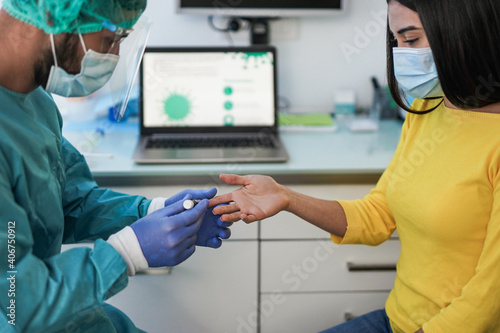 Male doctor making blood sugar test to a young woman in medical clinic for diabetes - Medical worker and patient wearing surgical face masks for coronavirus outbreak