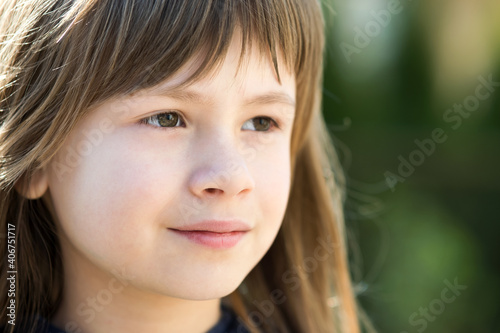 Portrait of pretty child girl with gray eyes and long fair hair outdoors on blurred bright background. Cute female kid on warm summer day outside.