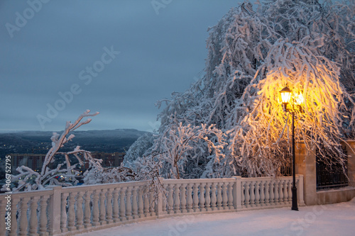 View from the balcony in the winter park in the evening on the city and mountains. The lantern illuminates the area covered with snow. Mashuk, Pyatigorsk. High quality photo