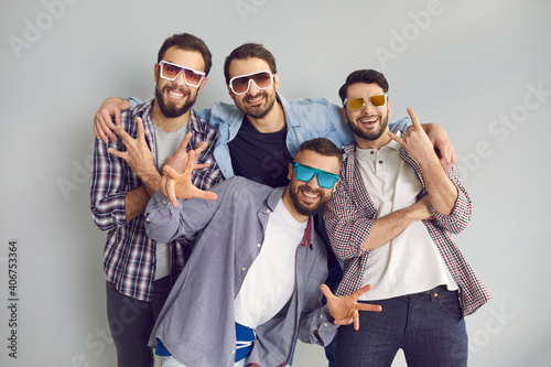 Happy best friends having fun while hanging out together. Group of 4 young men in sunglasses smiling, looking at camera and posing for funny photo in studio with light gray background photo